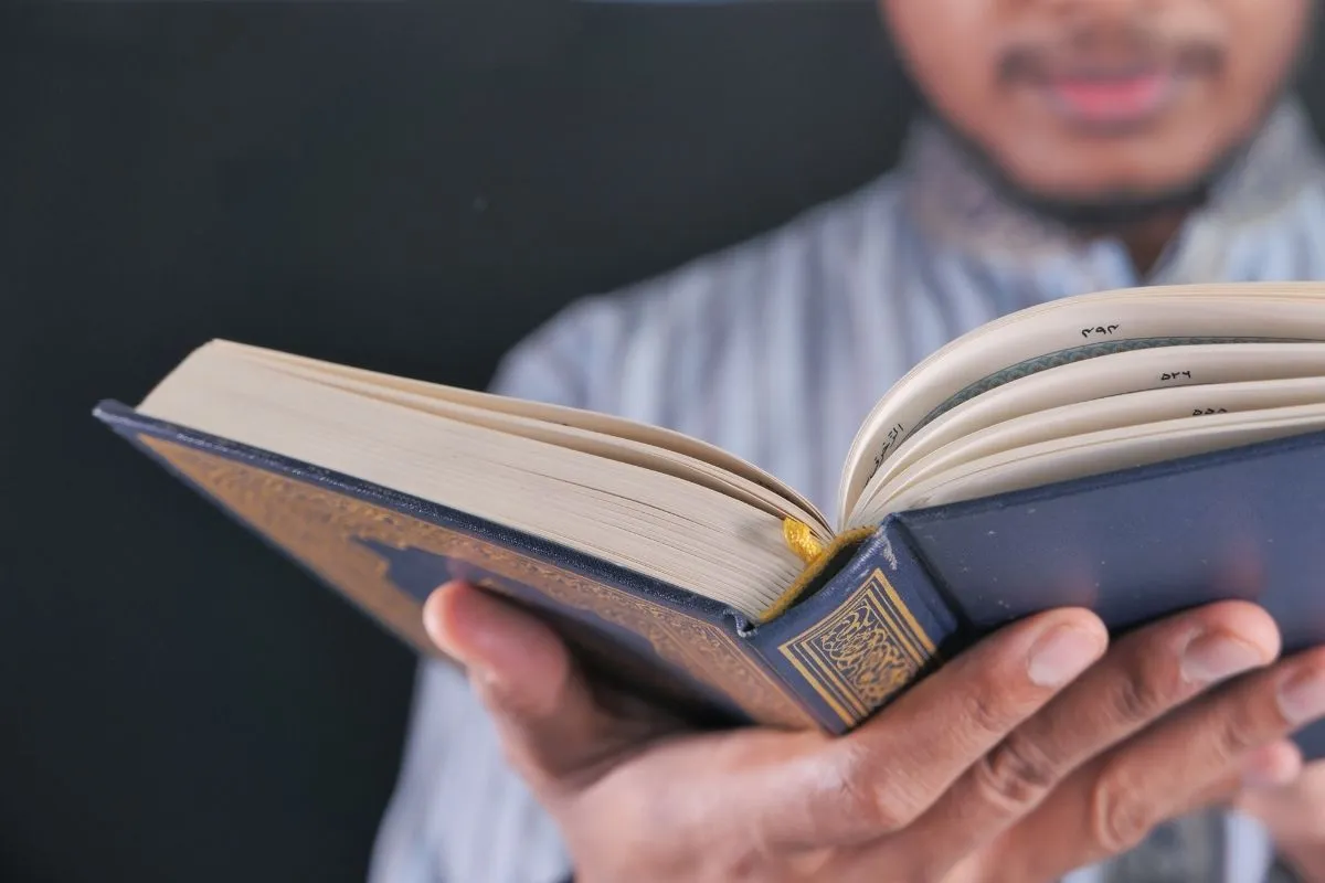 A teacher holding an open Mushaf